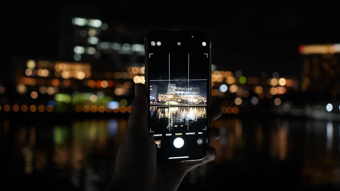 Tangan memegang ponsel dengan lampu kota malam yang blur di latar belakang