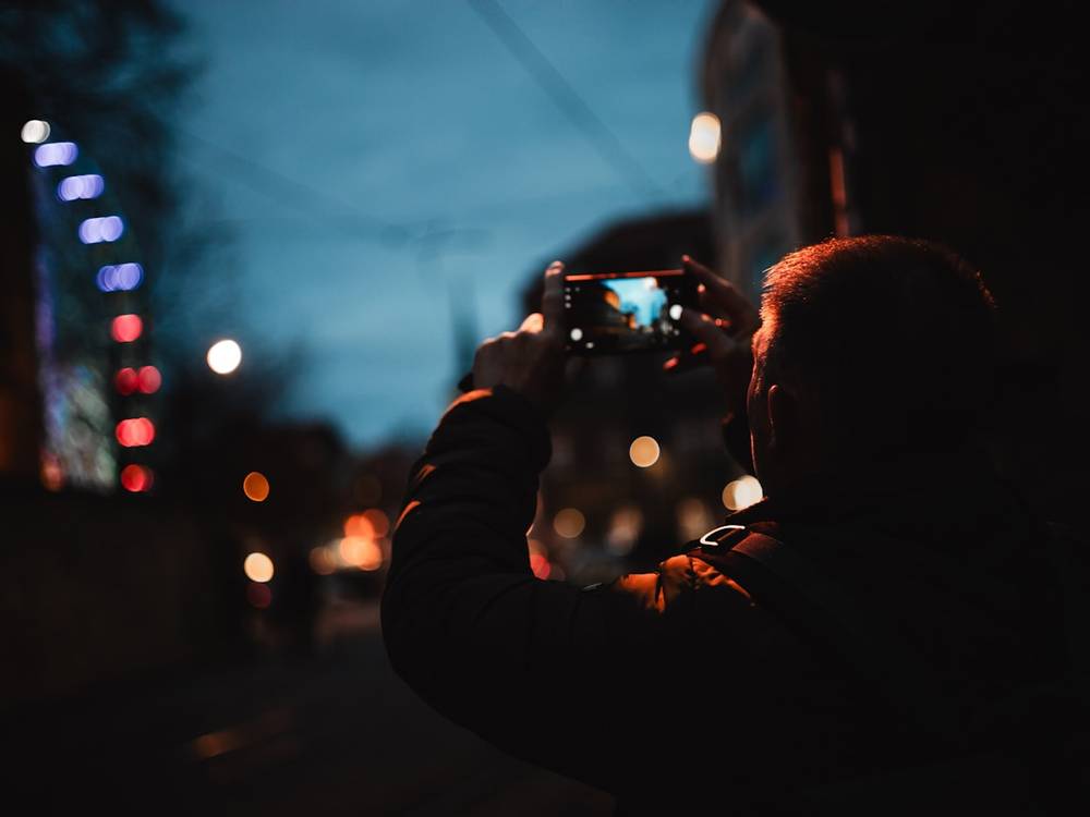 Pria memegang ponsel di malam hari dengan lampu kota blur
